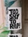 A weathered poster with bold black lettering reads 'Too Shy To Rap!' pasted on a metal pole amidst peeling layers of old advertisements. Green leaves from a nearby plant partially cover the bottom of the poster.