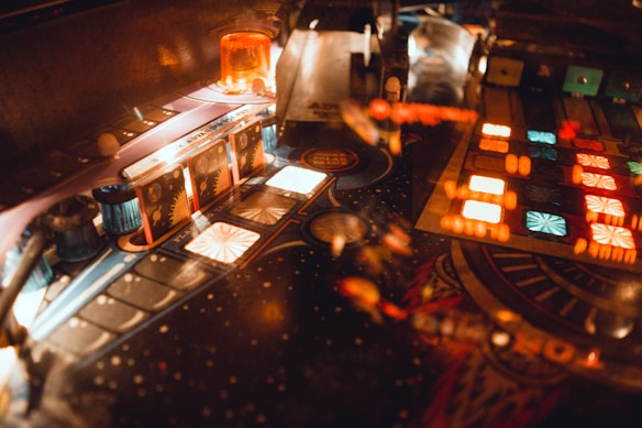 A pinball machine with vibrant, illuminated features including various colorful lights and intricate mechanical components. The board is adorned with symmetrical patterns and glowing sections, adding to the dynamic atmosphere.