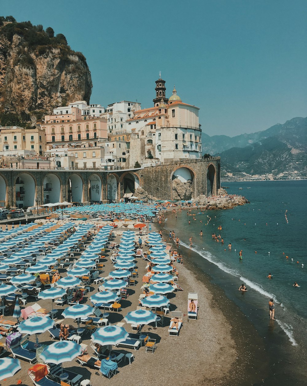 Lotto di ombrelloni da spiaggia blu e bianchi vicino al muro di cemento sotto il cielo sereno in riva al mare