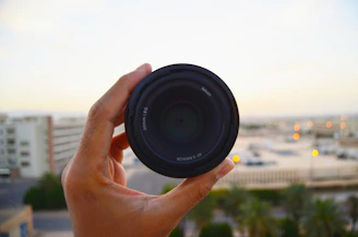 Close-up of a hand holding a compact pepper spray canister with a blurred city background.