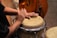 A person plays a conga drum with their hands, creating rhythmic beats. The drum has a natural skin top with a smooth texture, and the scene contains warm, earthy colors.