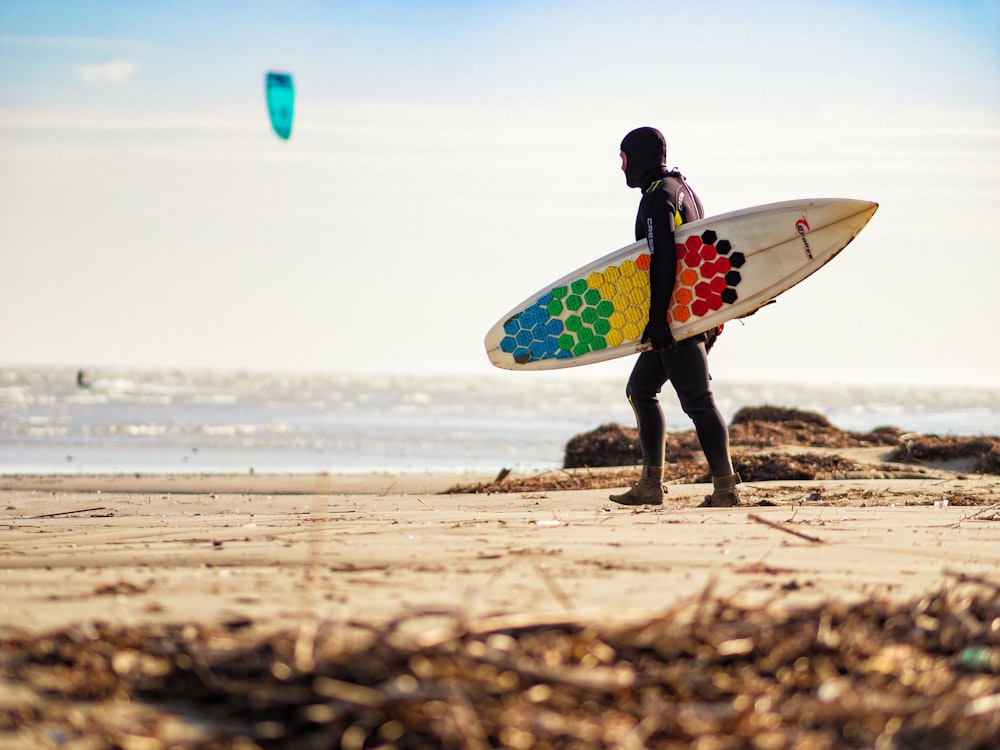 person carrying multicolored surfboard walking on seashore