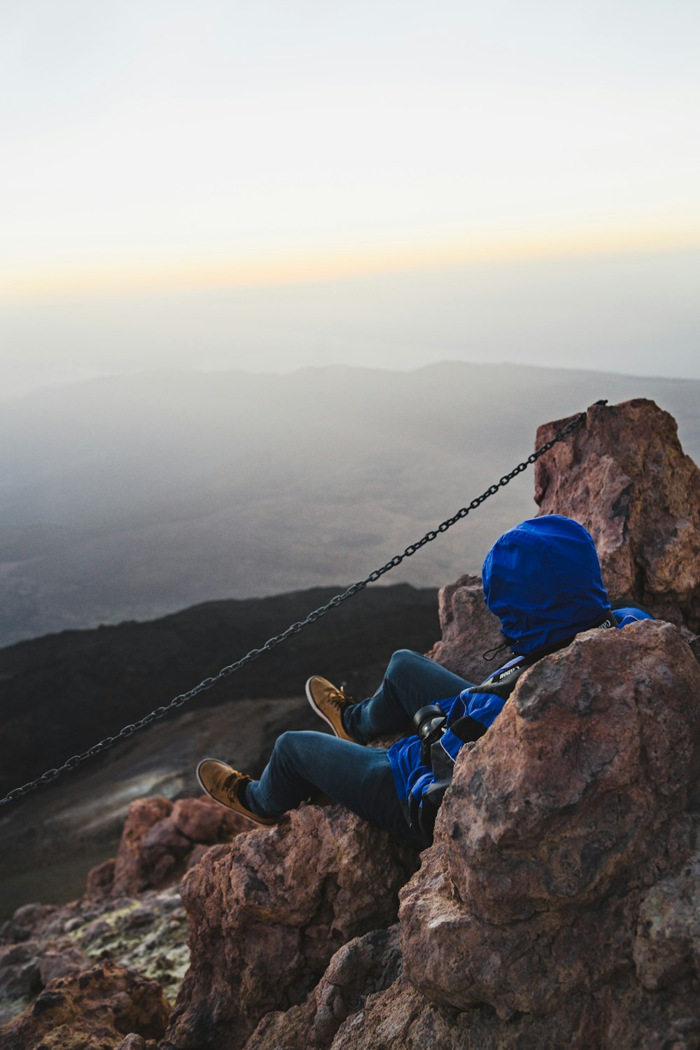 man sitting on cliff facing mountain