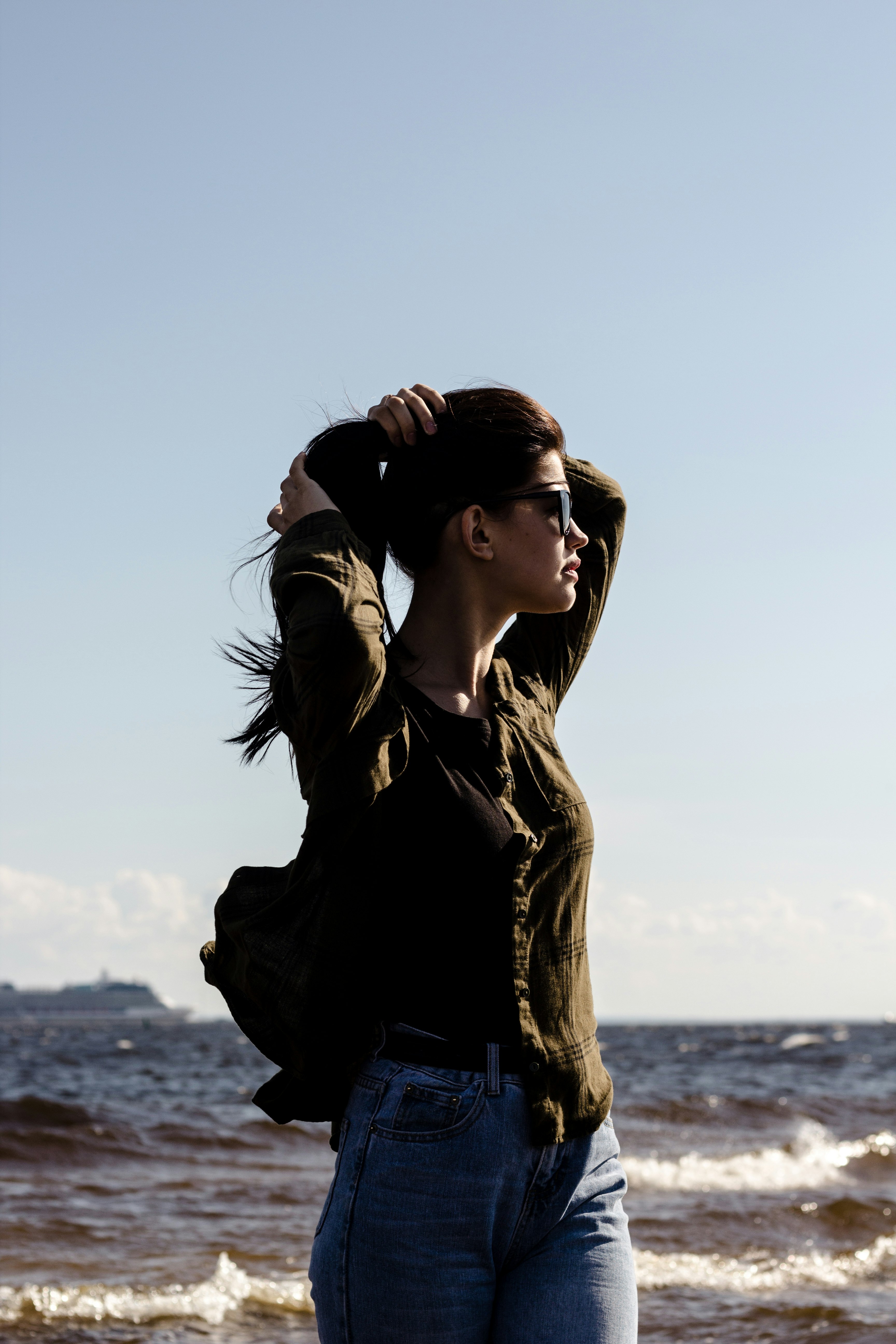 woman fixing hair while standing near body of water