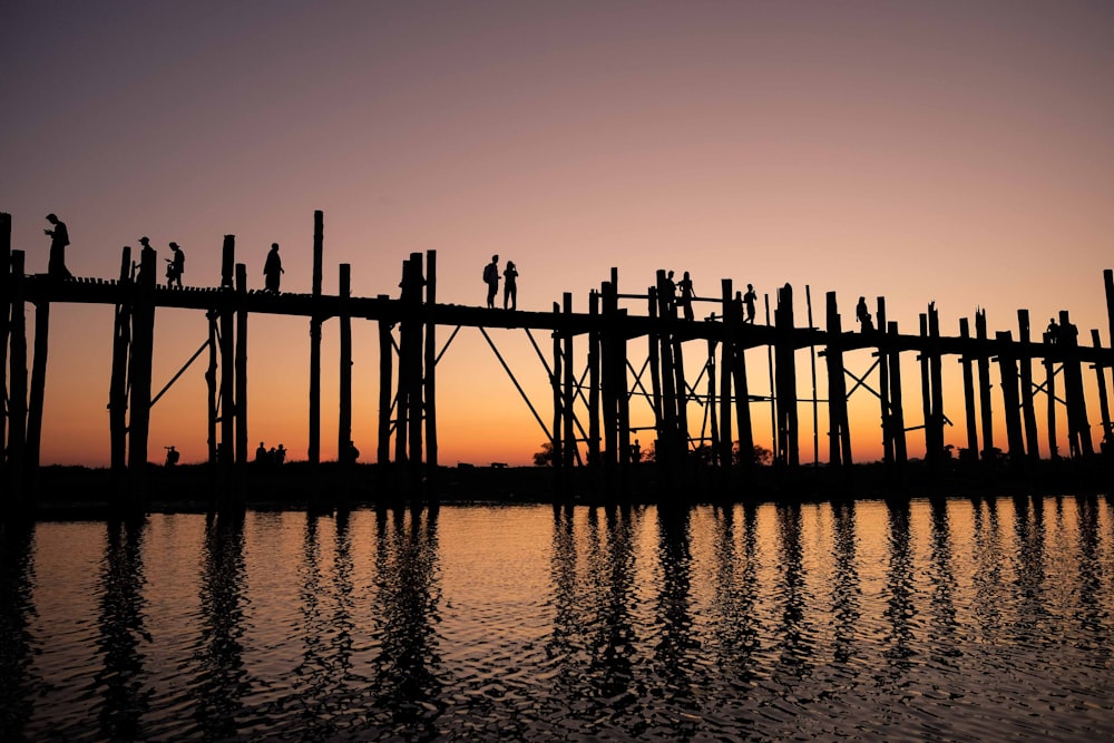 silhouette photograph of two person standing on wooden bridge during golden hour