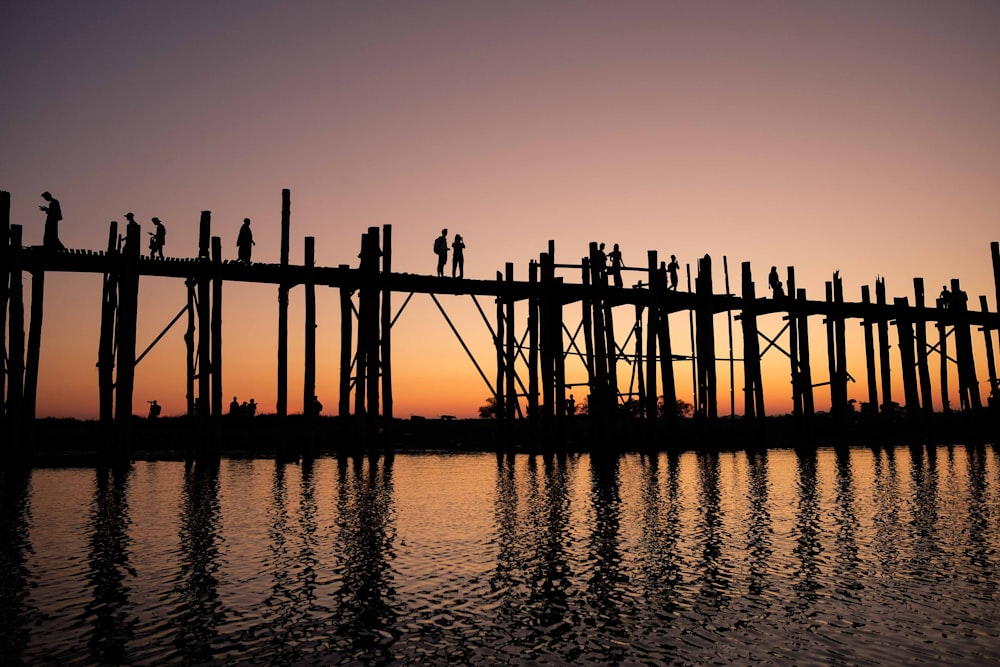 Silhouettenfoto von zwei Personen, die während der goldenen Stunde auf einer Holzbrücke stehen