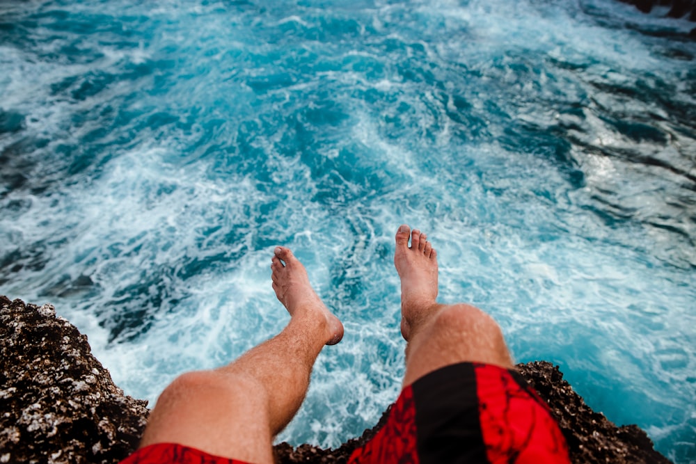 person sitting on brown cliff near body of water