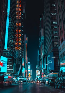 street photography of vehicles traveling on road between large buildings during nighttime