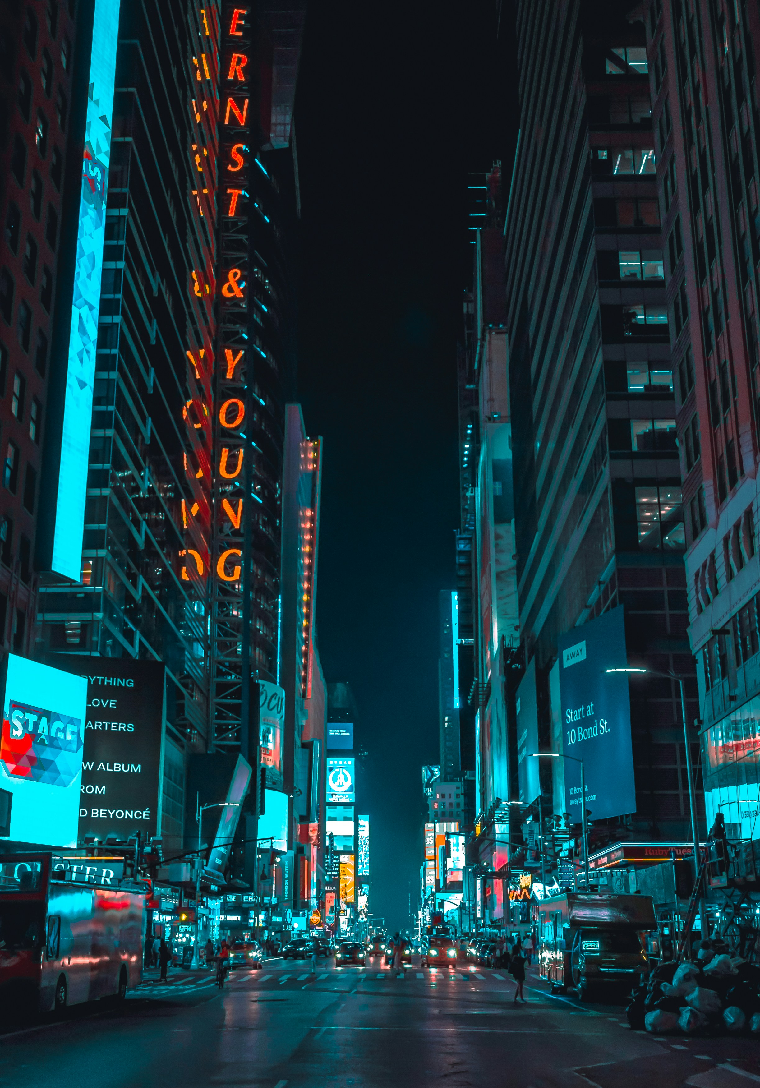 street photography of vehicles traveling on road between large buildings during nighttime