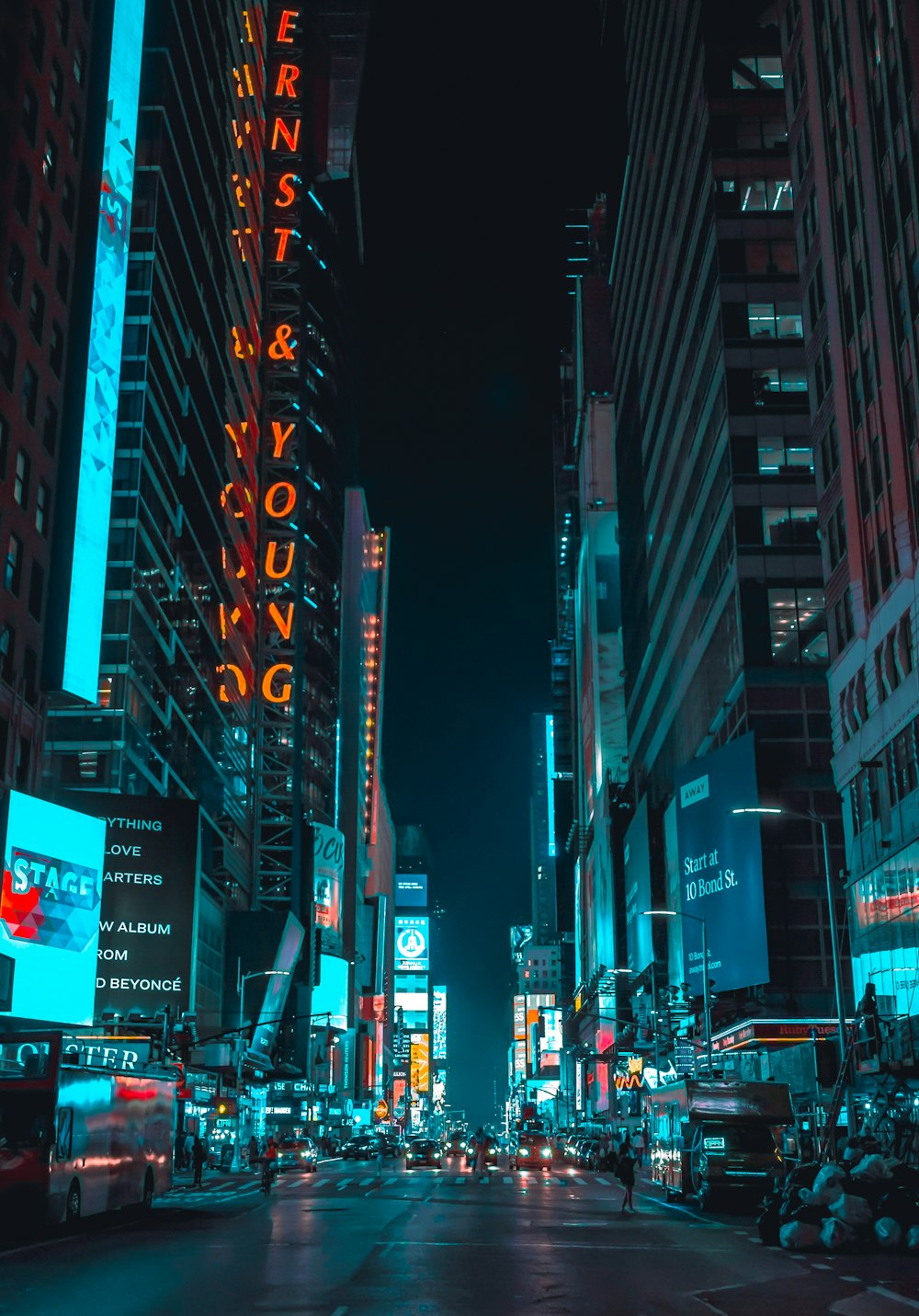 street photography of vehicles traveling on road between large buildings during nighttime