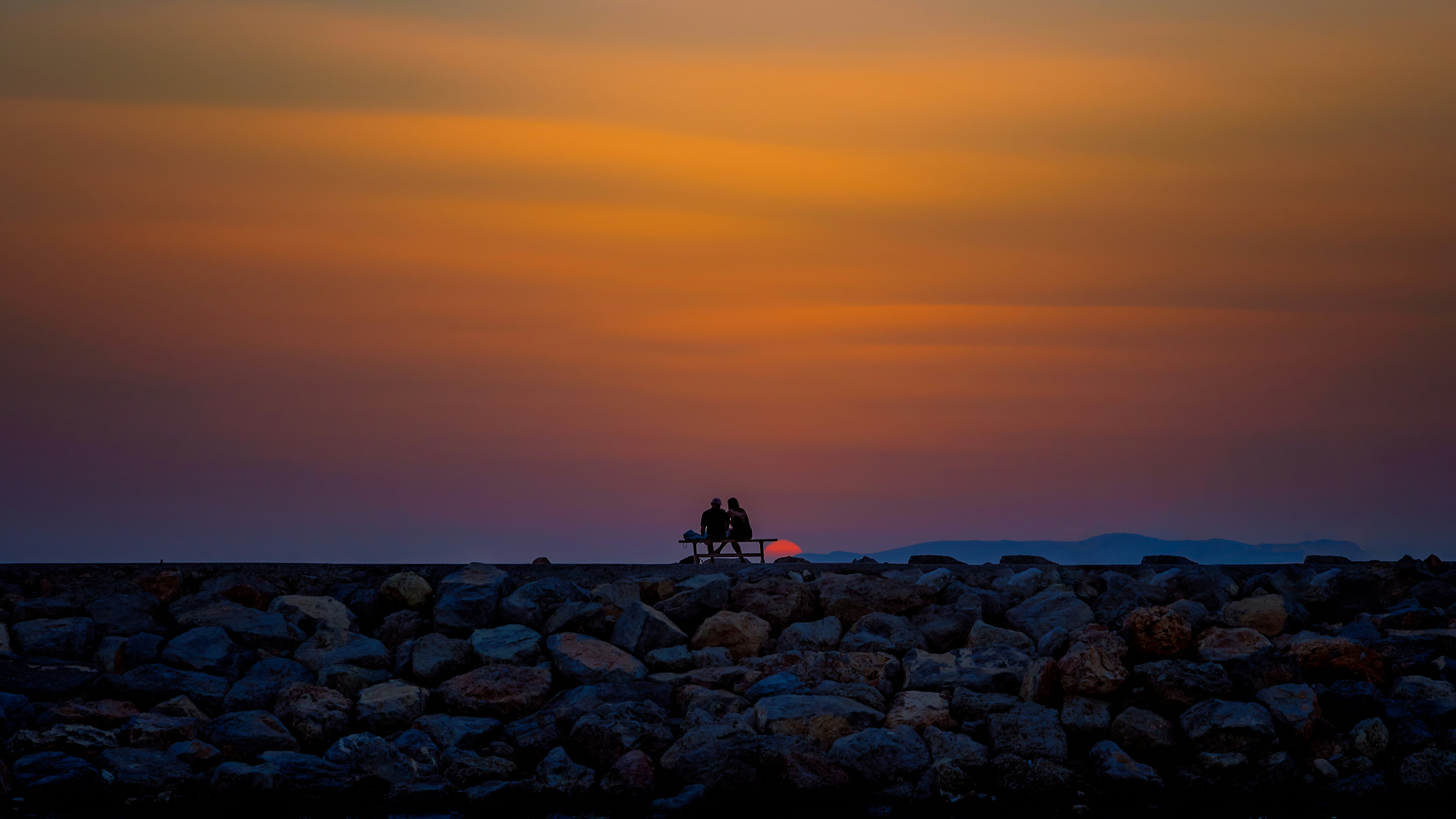 Two people sitting together at dusk, small against the expanse of the sky above and the earth beneath.
