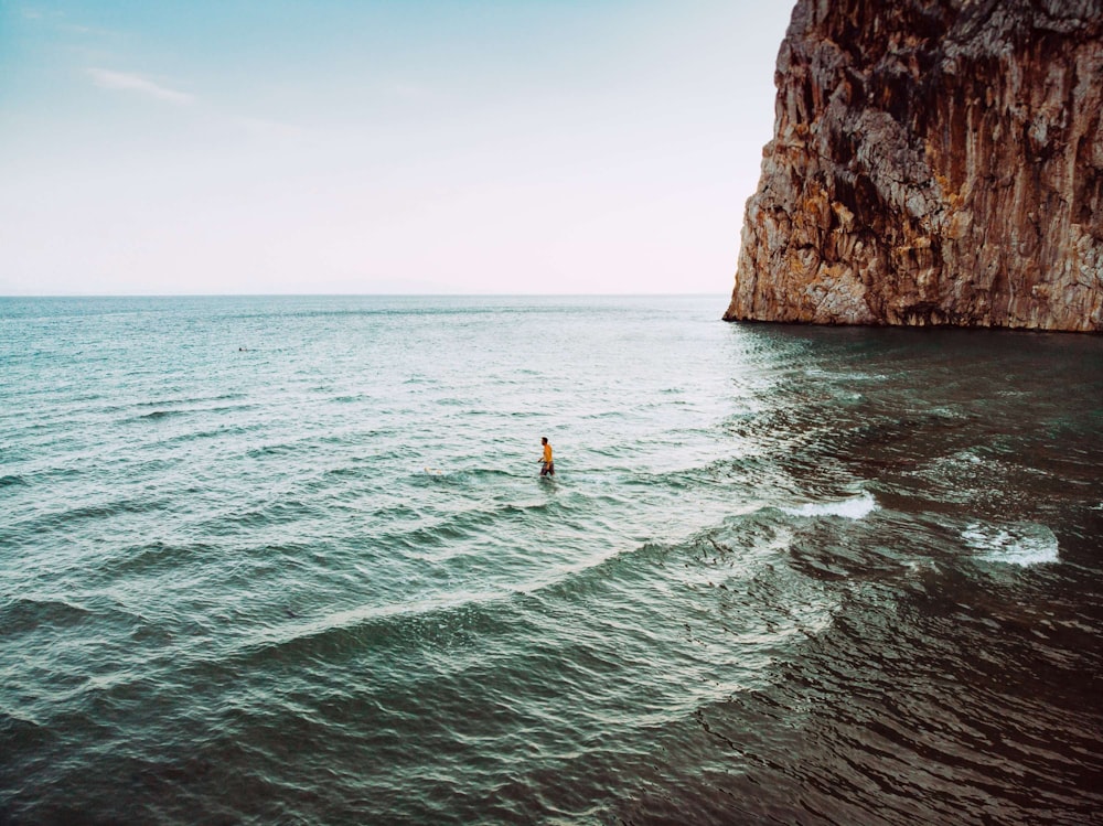 person on body of water beside rock