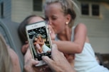 person taking a picture of girl kissing woman