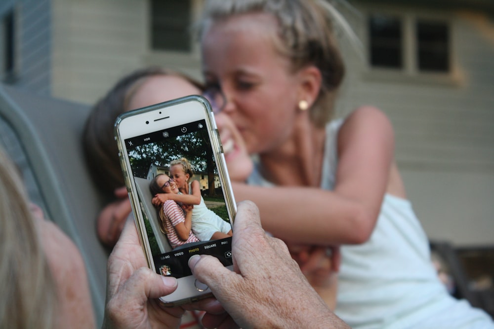 person taking a picture of girl kissing woman