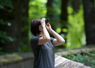 selective photography of woman holding binoculars looking upward outdoors