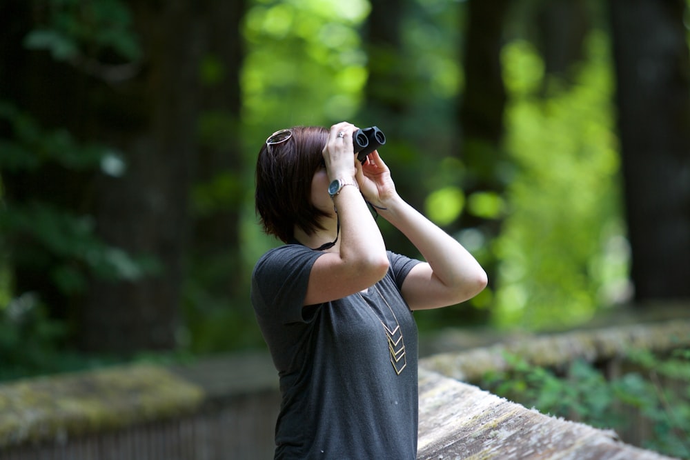 selective photography of woman holding binoculars looking upward outdoors