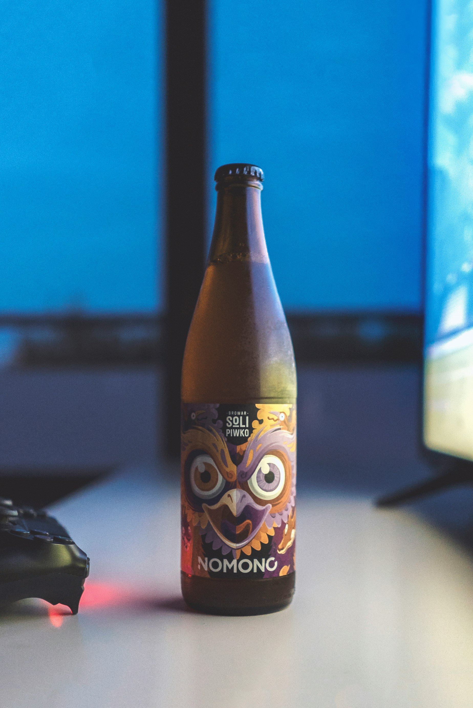 tilt-shift lens photography of Nomono beer bottle in-front of a flat screen TV