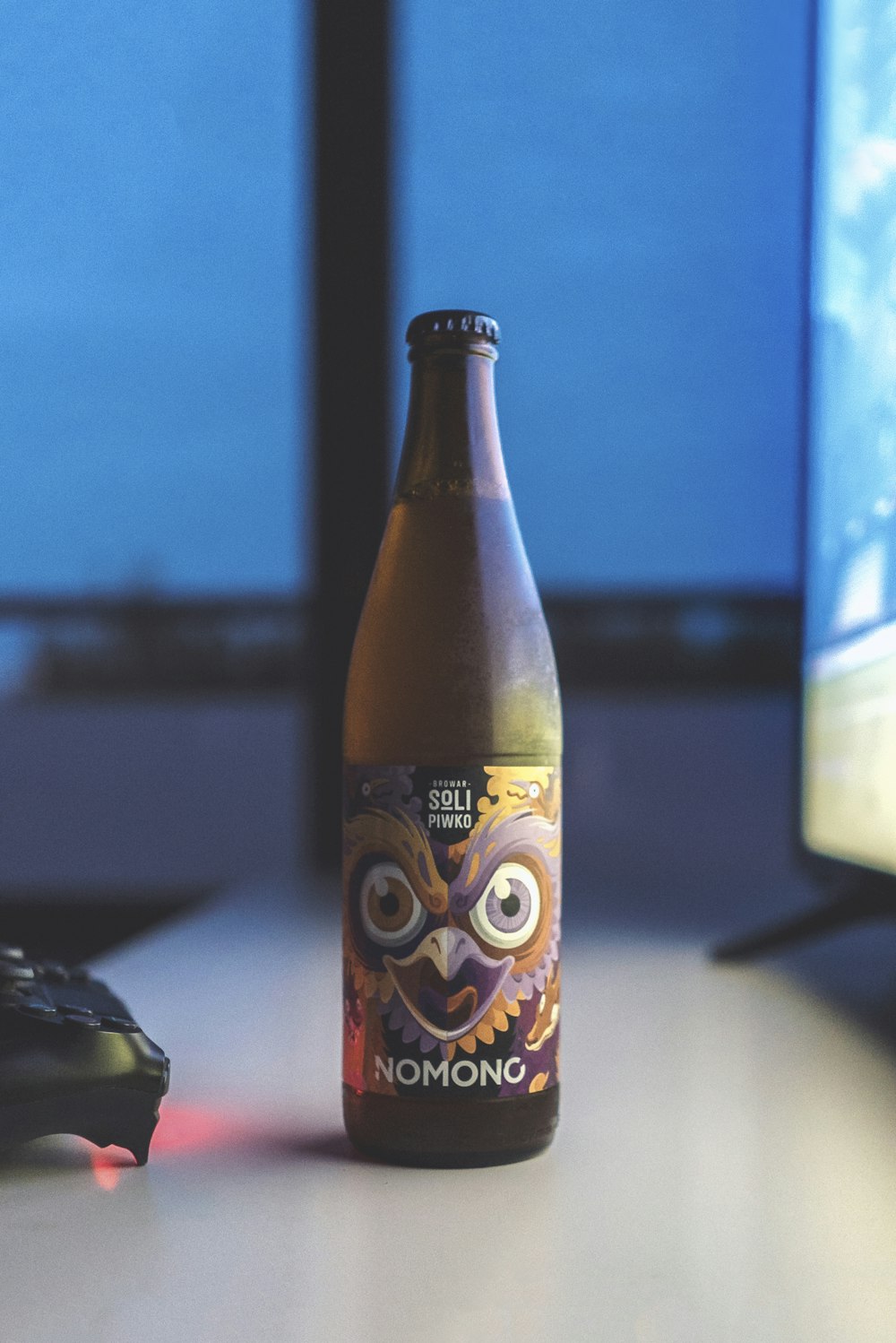 tilt-shift lens photography of Nomono beer bottle in-front of a flat screen TV