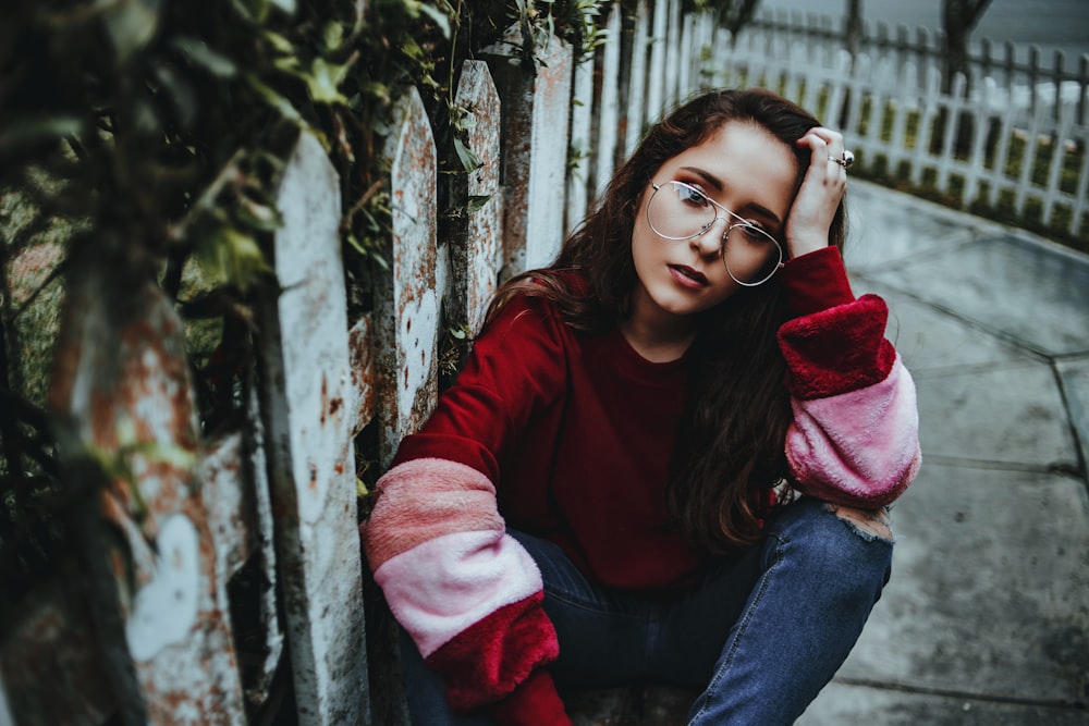 a woman sitting on the ground next to a fence