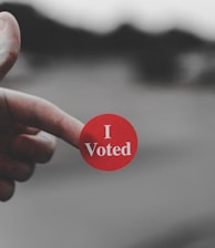 a hand holding a red button that says i vote