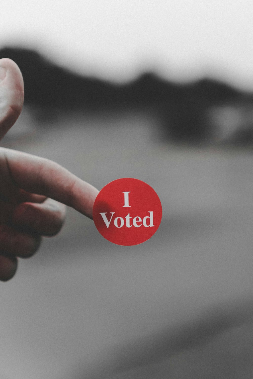 「I vote」と書かれた赤いボタンを持つ手