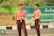 Two young individuals are wearing scout uniforms, including beige shirts and brown pants, with red and white striped scarves. They are standing outdoors near a road with signage in the background, suggesting a possible school or community event.