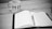 A black and white image of a notebook open on a desk, with a pen placed on top of it. To the left, there is a mug with the word 'MIND DESIGN' printed on it. The environment suggests a workspace or study area.