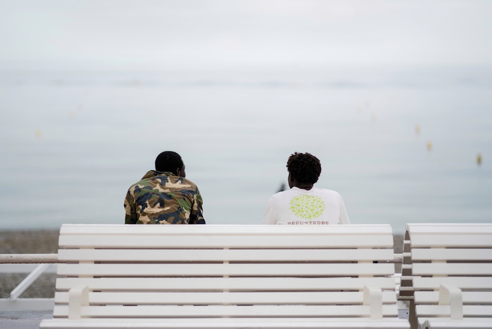 two men sitting on bench facing sea