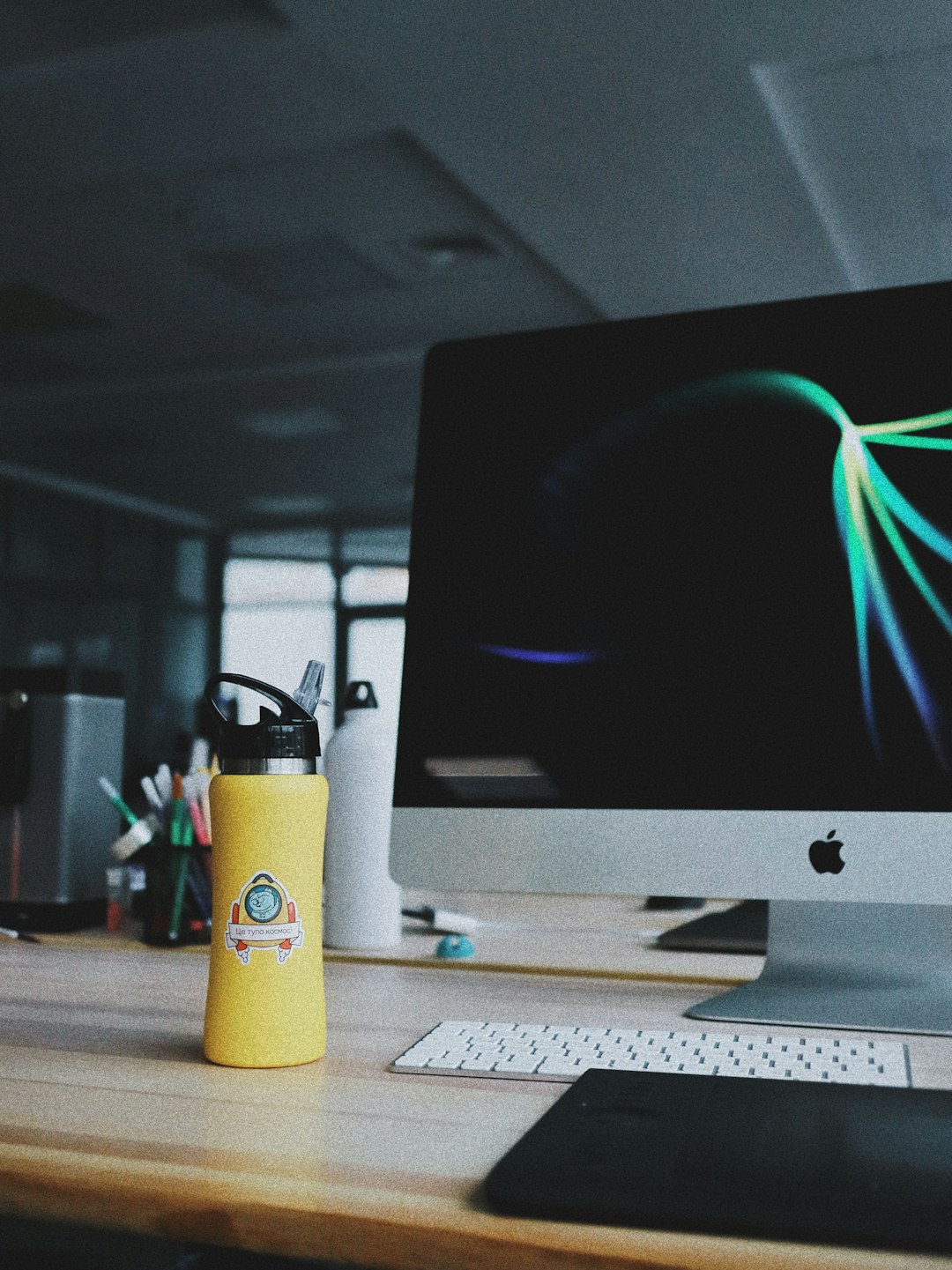 powered on silver iMac beside yellow tumbler