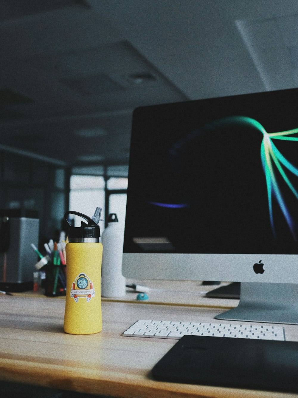 powered on silver iMac beside yellow tumbler