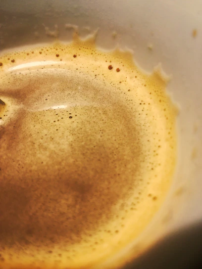 Close-up of a steaming cup of golden coffee with swirling cream on top