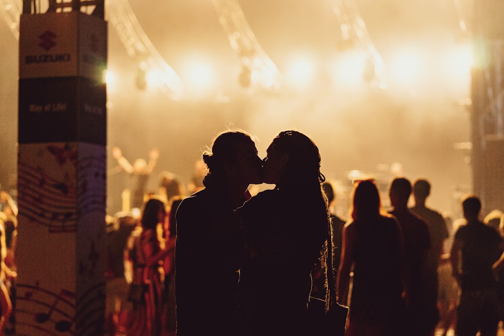 man and woman kissing in the middle of concert