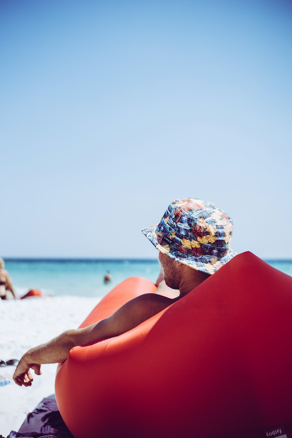 man lying on red banana bed near beach