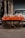 A street vendor setup with plastic bags filled with various grains and snacks displayed on a table covered with a vibrant orange cloth. The table is part of a cart with visible bicycle wheels, parked on a street in front of a closed shop shutter. The scene captures an urban marketplace atmosphere.