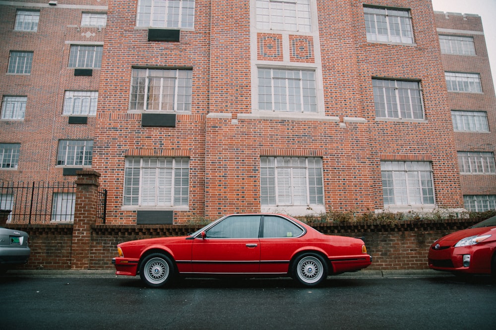 red coupe parked beside brown building