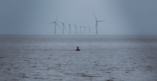 person swimming on water near windmills in Crosby Beach United Kingdom