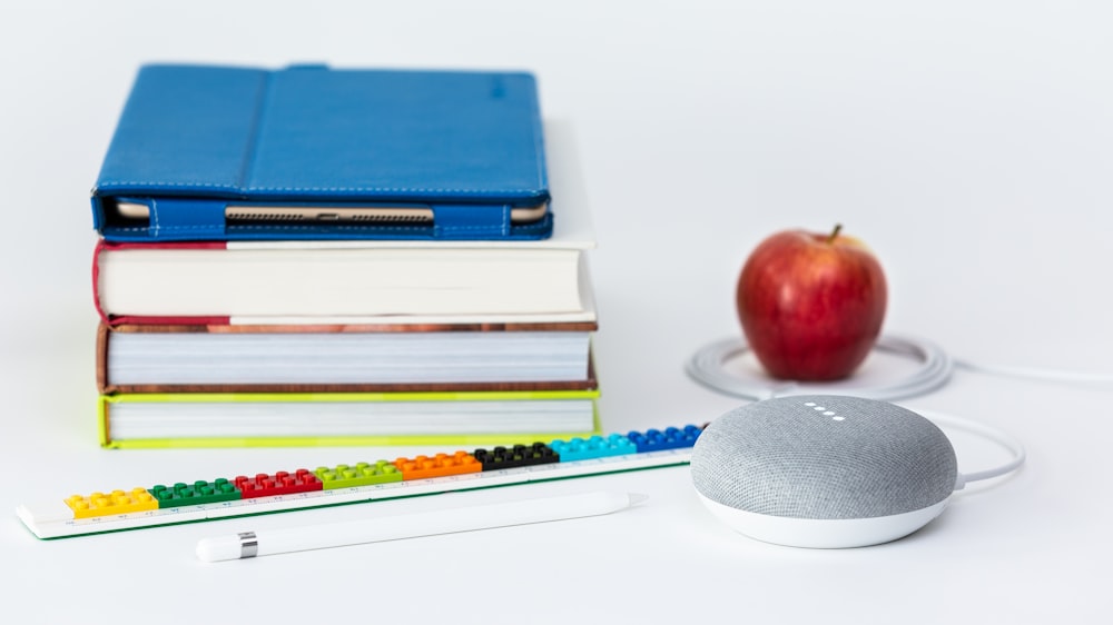 fruta de maçã crocante perto de livros e giz Google Home Mini alto-falante inteligente