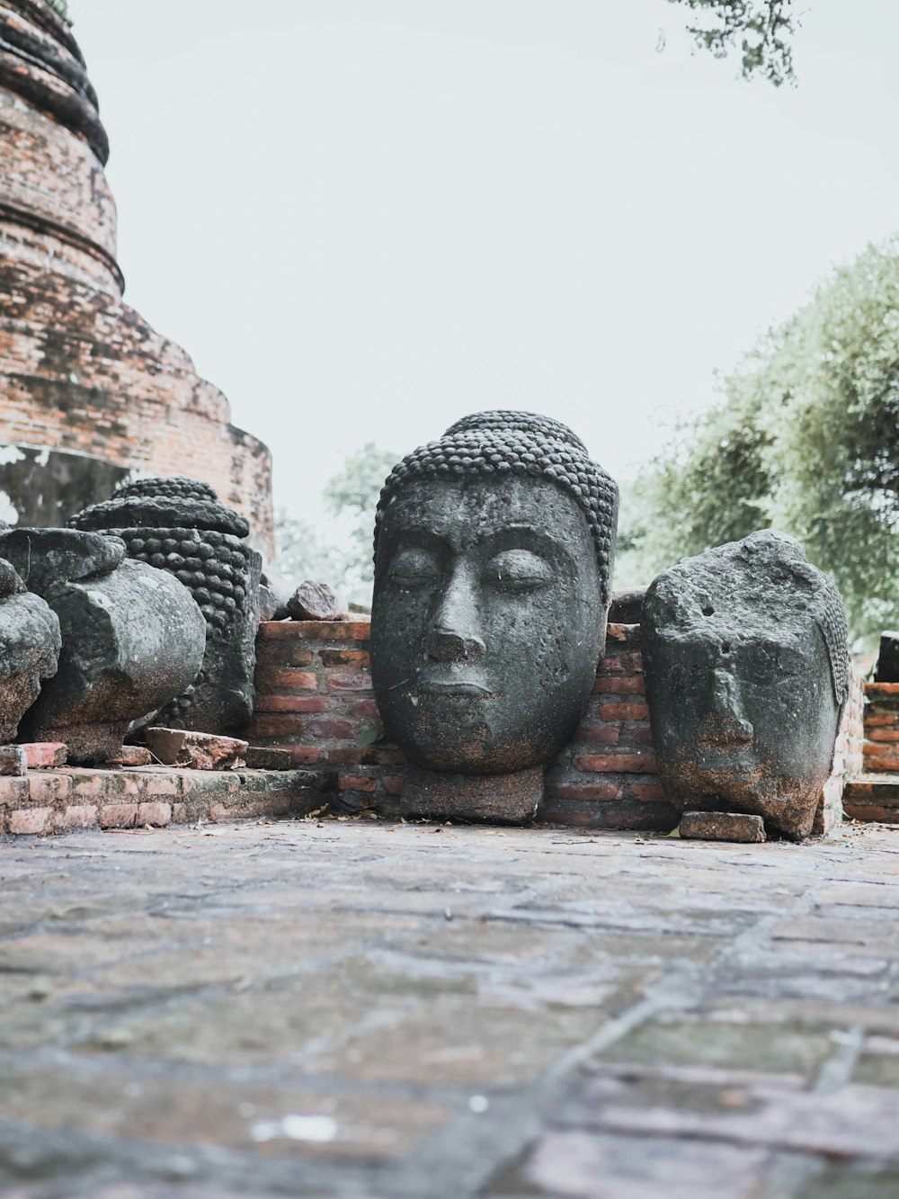Buddha head statue beside brown brick wall at daytime