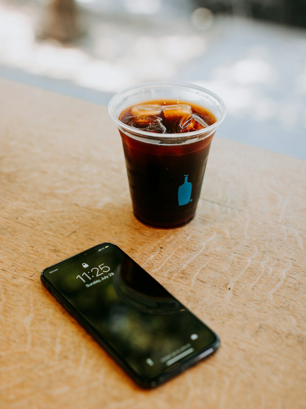 角氷入り飲料で満たされた透明な使い捨てカップの横にある黒いiPhone 7