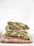 A close-up of two halved pita sandwiches filled with fresh greens, avocado slices, and sprouts. They are stacked on a wooden board with a minimalist background, creating a focus on the natural textures and colors of the ingredients.