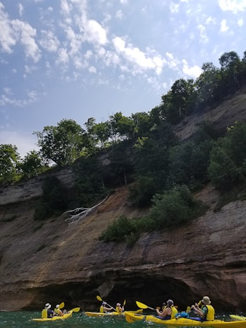 A group of young adventure seekers kayaking between towering fjord cliffs under a soft spring sky.