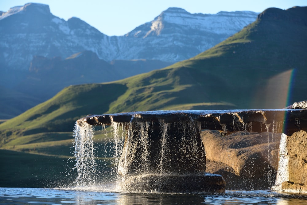 black rock formation with water flowing on top falls to the body of water at daytime