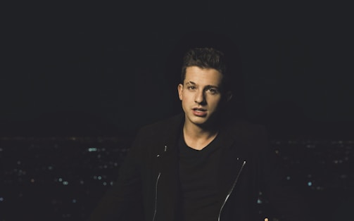 Model wearing a dark minimalist jacket standing against an urban nighttime backdrop