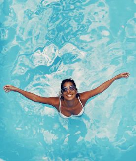 Happy woman relaxing by her pool with clear blue water on a sunny day.
