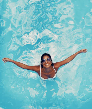 Happy woman relaxing by her pool with clear blue water on a sunny day.