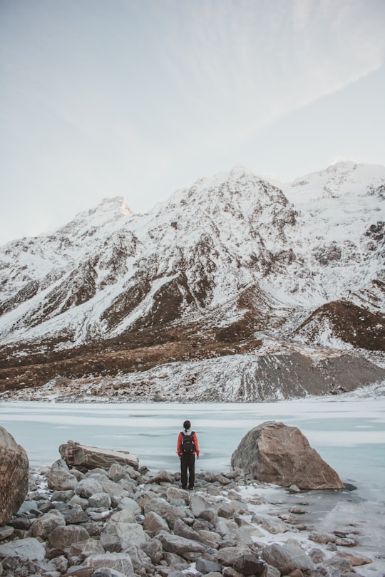 person standing beside rock facing mountain in Mount Cook New Zealand