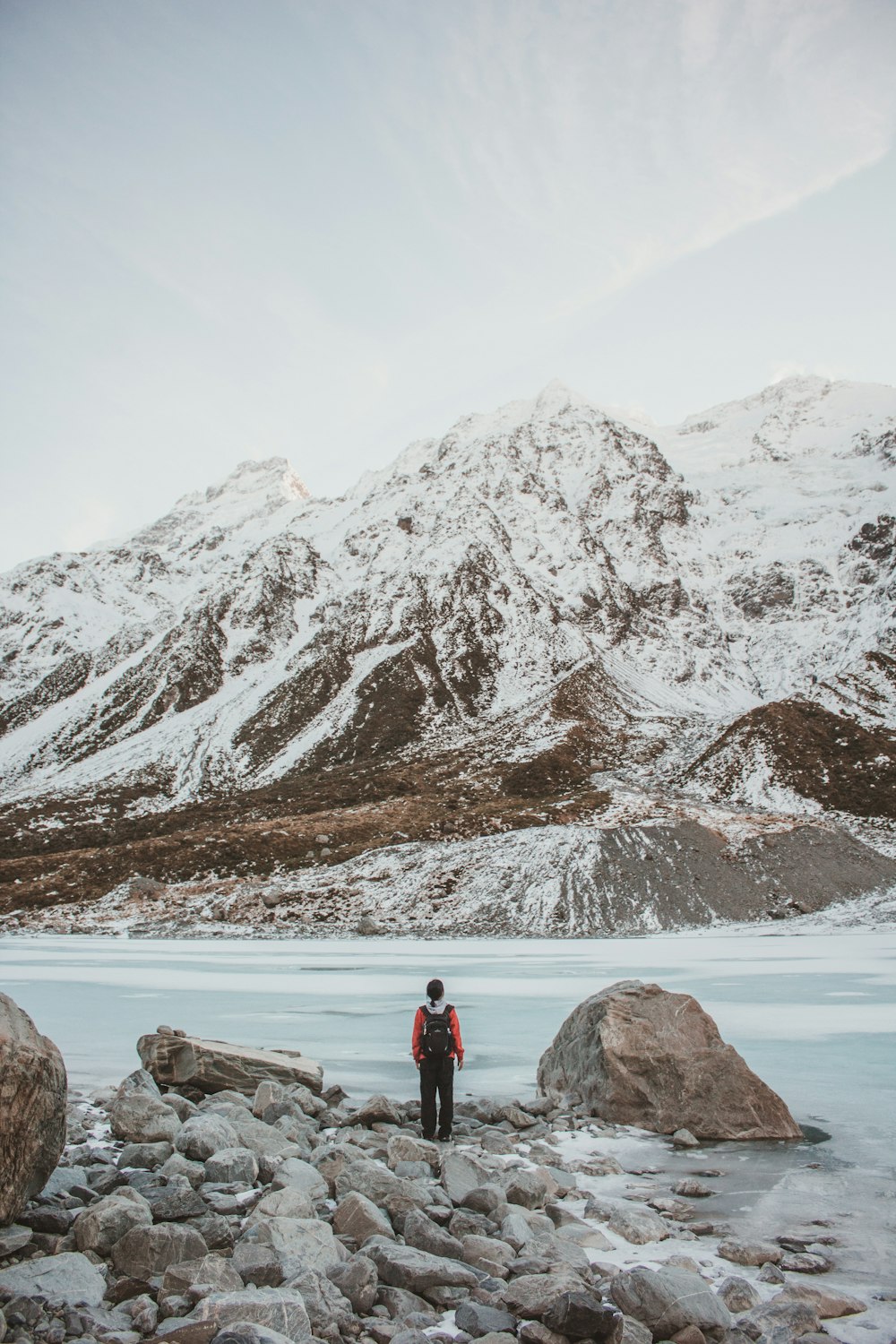 person standing beside rock facing mountain