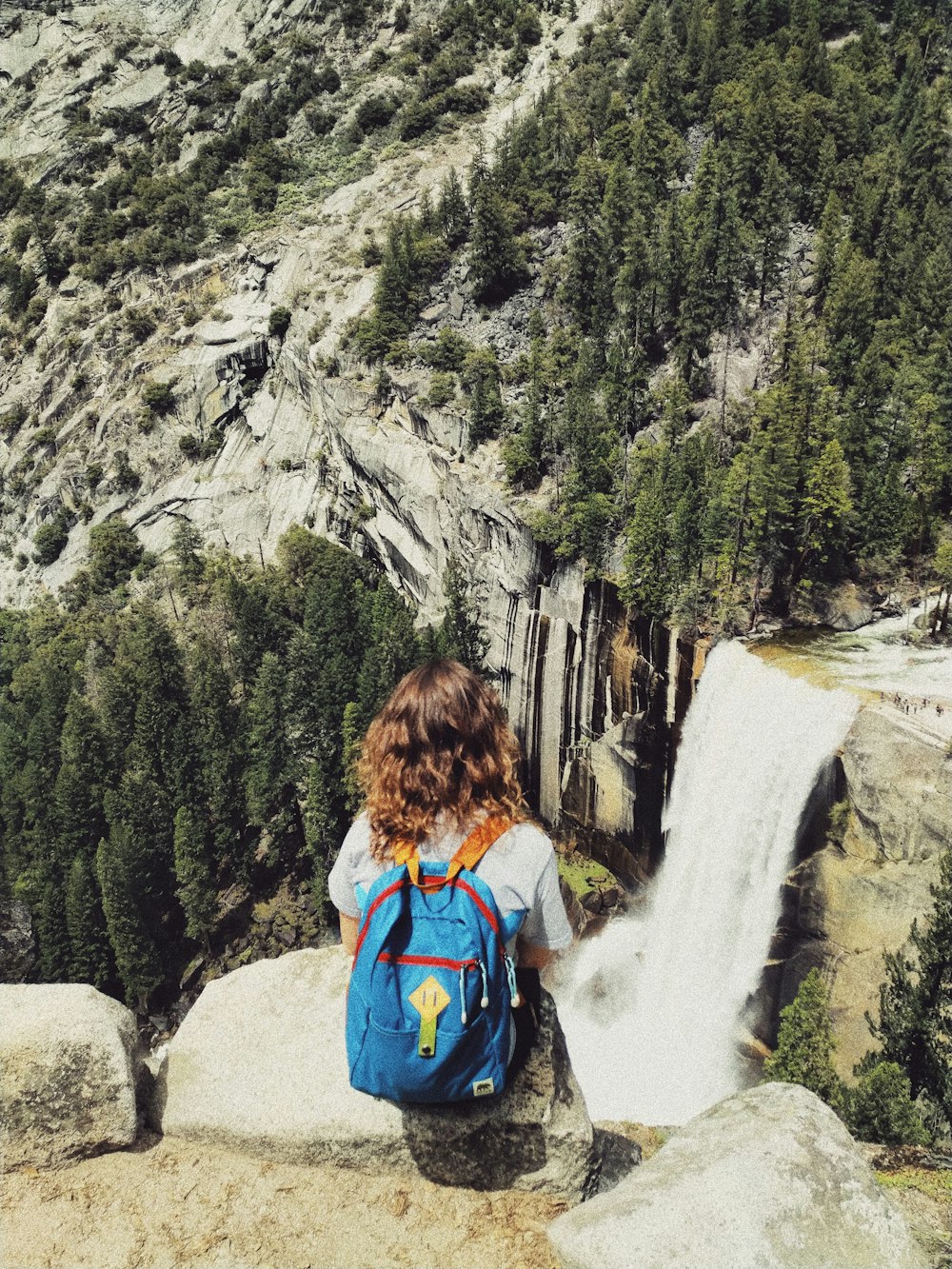 Frau sitzt auf grauem Felsen über Wasserfällen