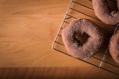 Three sugar-coated baked goods resembling donuts are placed on a wire cooling rack, positioned at an angle on a wooden surface.