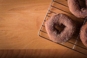 Three sugar-coated baked goods resembling donuts are placed on a wire cooling rack, positioned at an angle on a wooden surface.